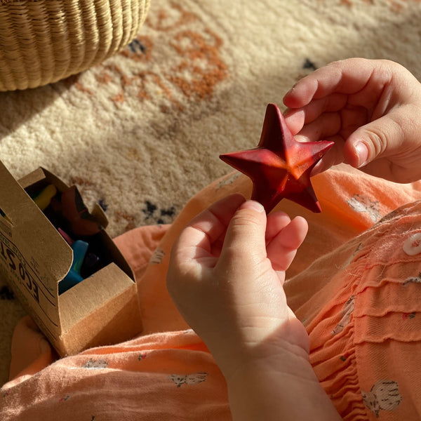 Eco-friendly 100% recycled star shaped red and orange swirled crayon, held in a child's hand..